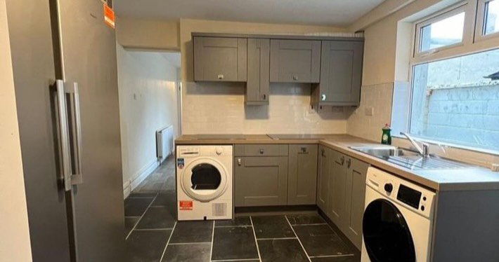 Modern kitchen with gray cabinets, slate floor, washing machine, and window.