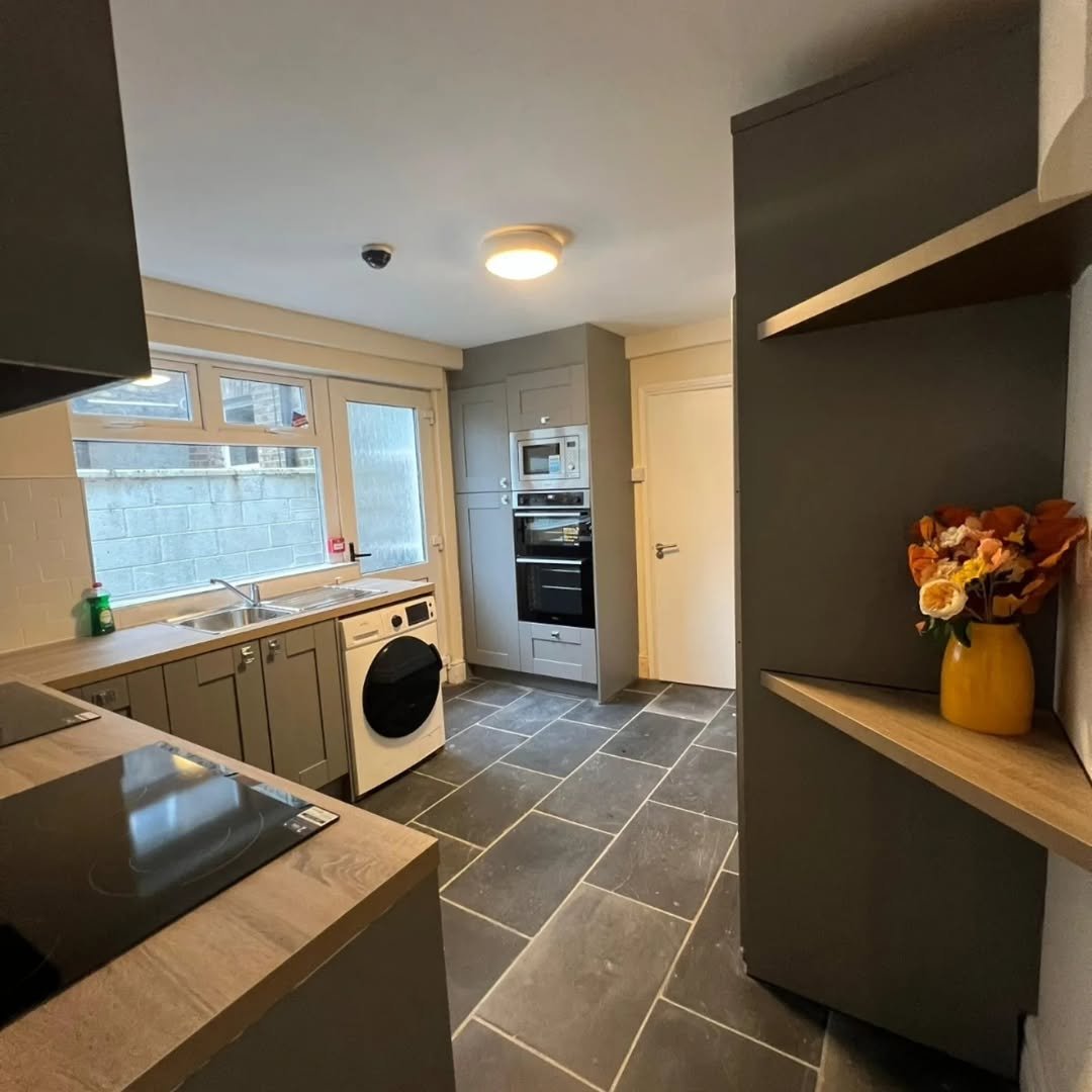 Modern gray kitchen with dark slate floors, integrated appliances, and washing machine under window.
