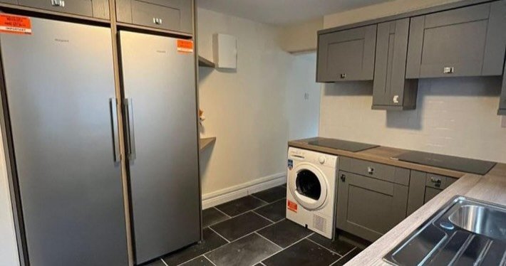 Modern gray kitchen with stainless steel appliances and dark flooring.