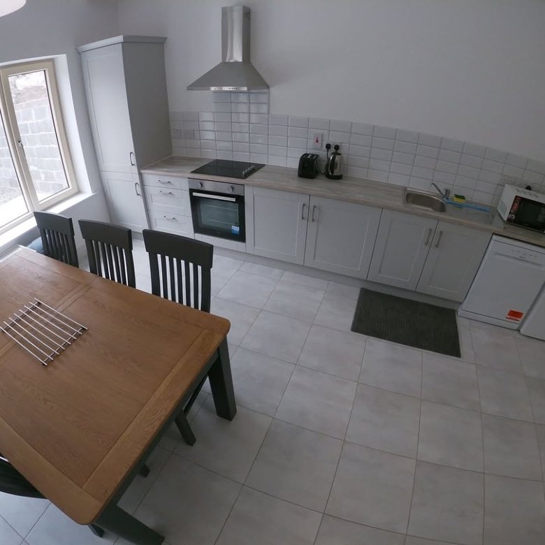 Modern kitchen with gray cabinets, stainless steel appliances, and a wooden dining table with black chairs.