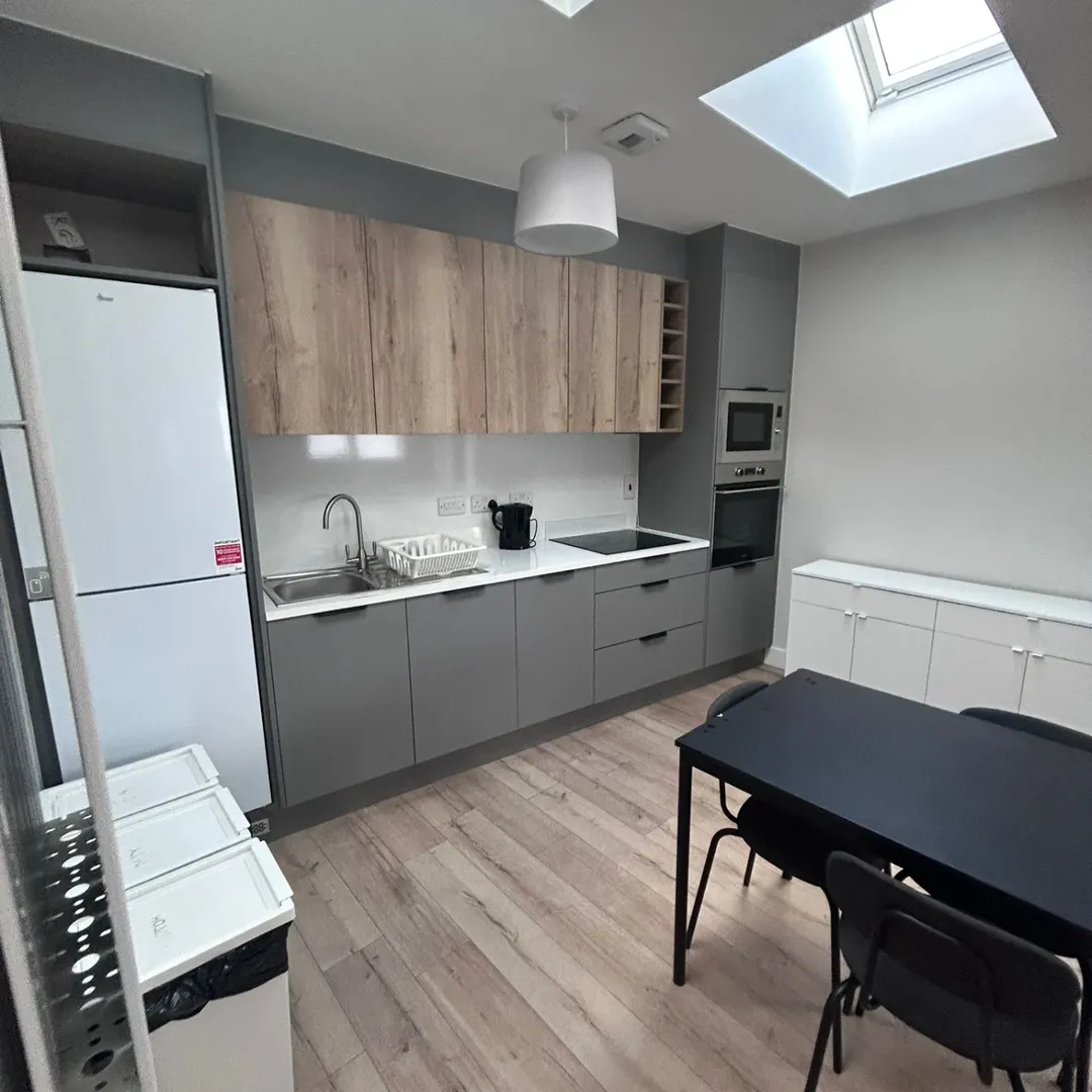 Modern kitchen with gray cabinets, wood accents, and skylight. Black table and chairs.