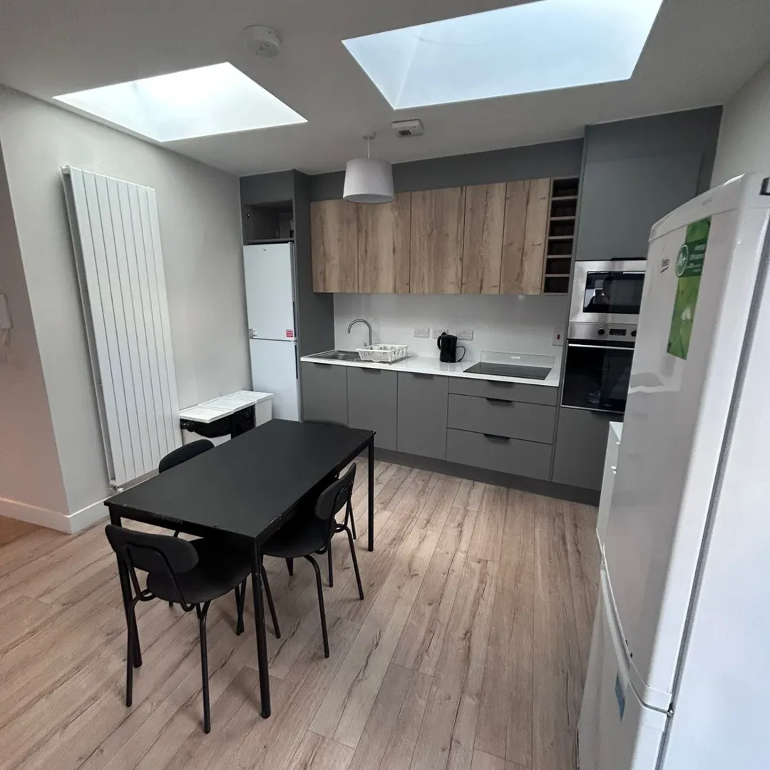 Modern kitchen with black dining table, grey cabinets, wood accents, and skylights in a brightly lit room.