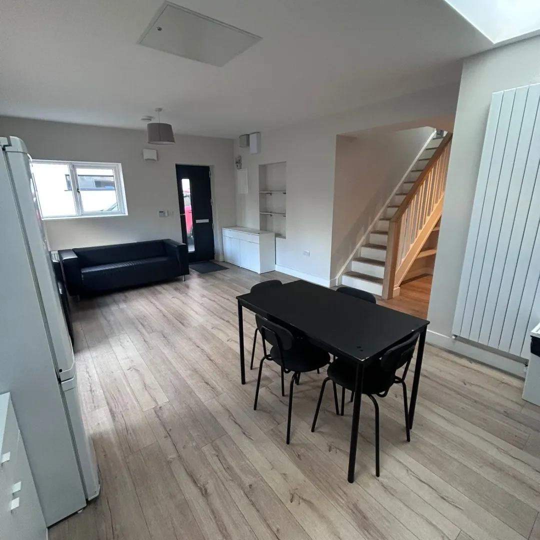 Living room with black dining set, sofa, stairs, and light wood flooring.
