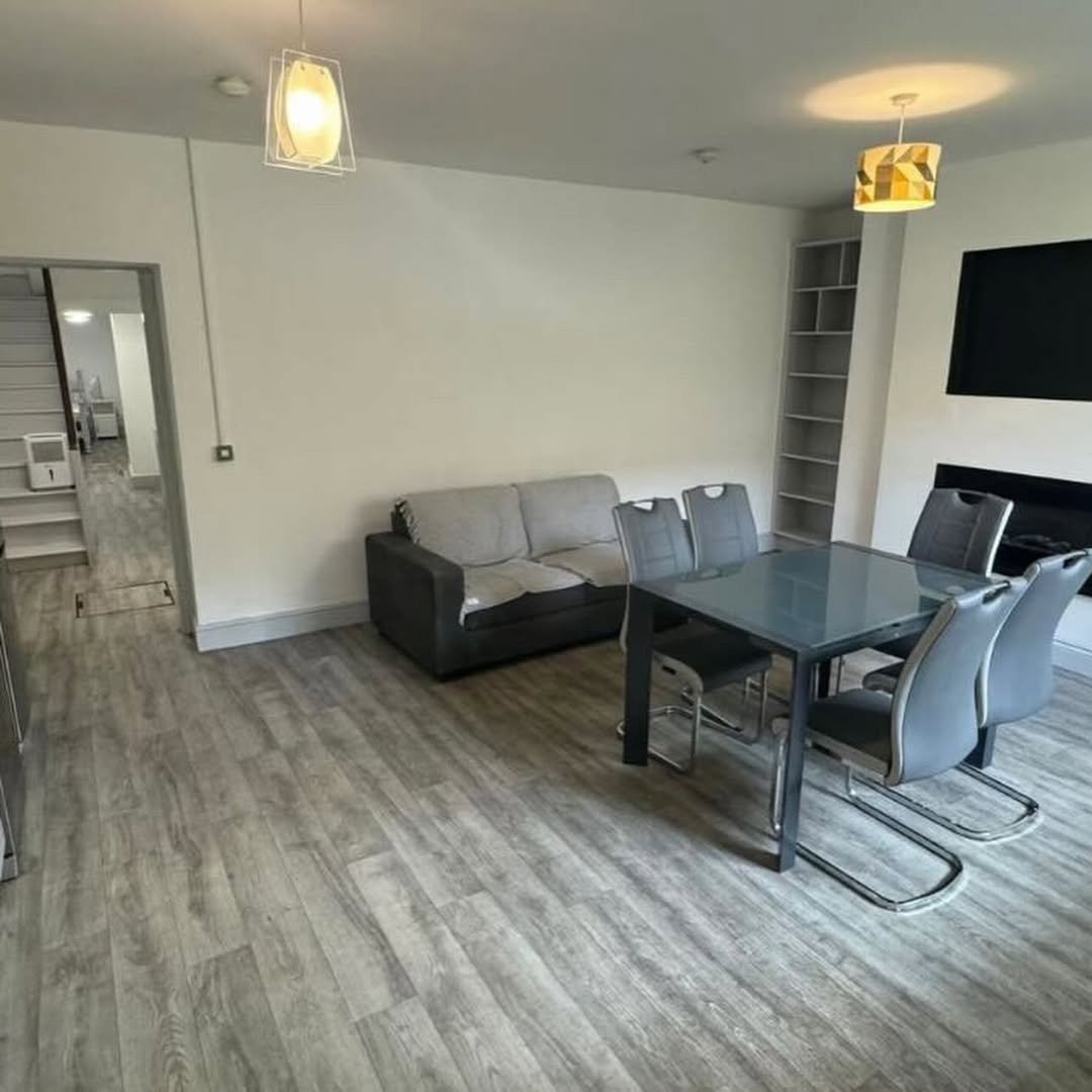Modern living room with gray sofa, dining table, and gray laminate flooring. Open floor plan with staircase.