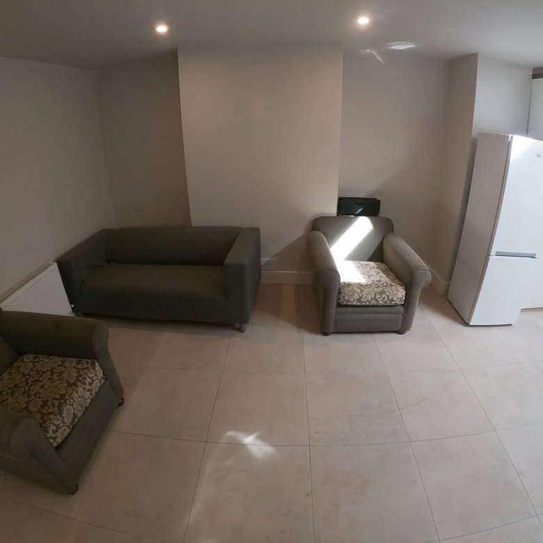 Living room with green sofa, armchair, fridge, and beige tile flooring. Modern interior design.