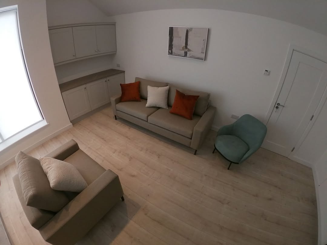 Living room with sofa, chair, built-in cabinets, and artwork. Light wood flooring, neutral tones, modern design.
