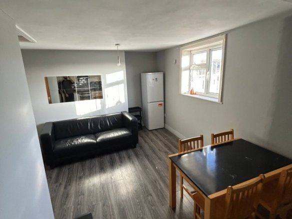 Living room with black sofa, dining table, fridge, and window with natural light. Modern interior design.