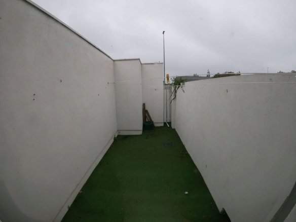 Narrow outdoor space with artificial turf, white walls, and clothesline.