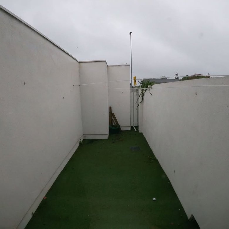Narrow outdoor space with artificial turf, white walls, and clothesline.