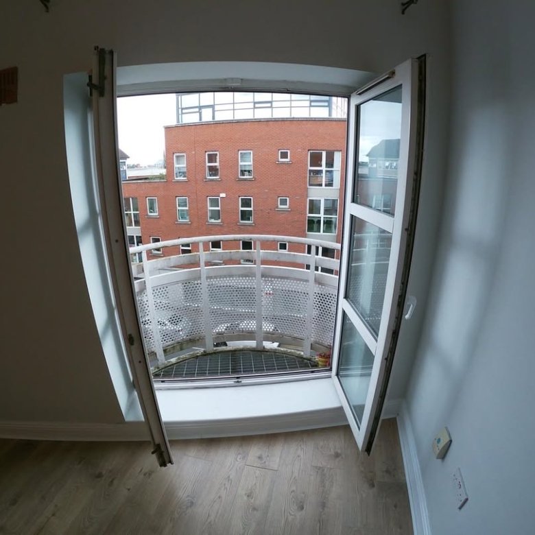 Open balcony door with view of brick building and white railing.