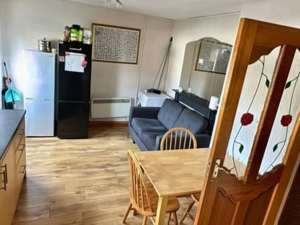 Open-plan kitchen and living area with fridge, sofa, and dining table.