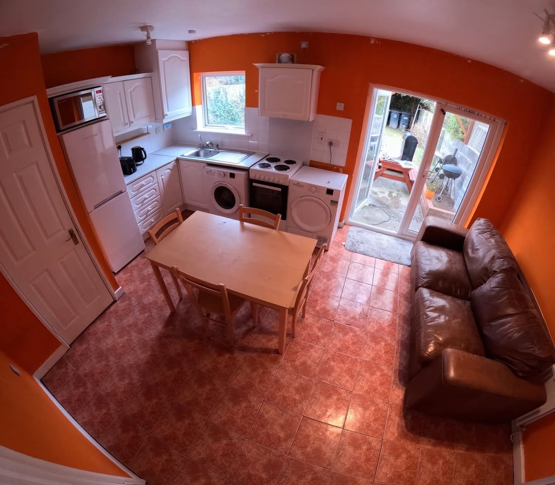 Cozy kitchen with table, brown sofa, and orange walls. Natural light from patio doors and window.
