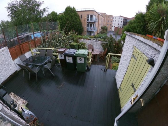 Outdoor deck area with bins, table, chairs, and greenery in a residential setting.