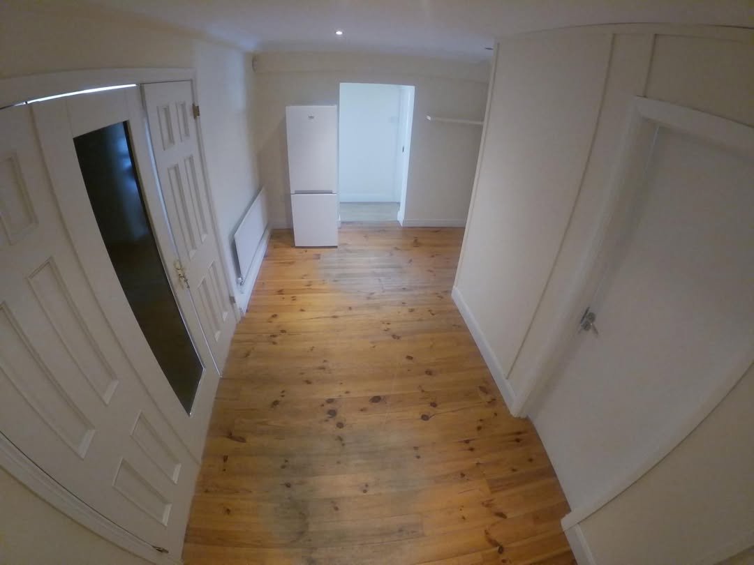 Interior view of a room with wooden floor, white walls, and appliances.