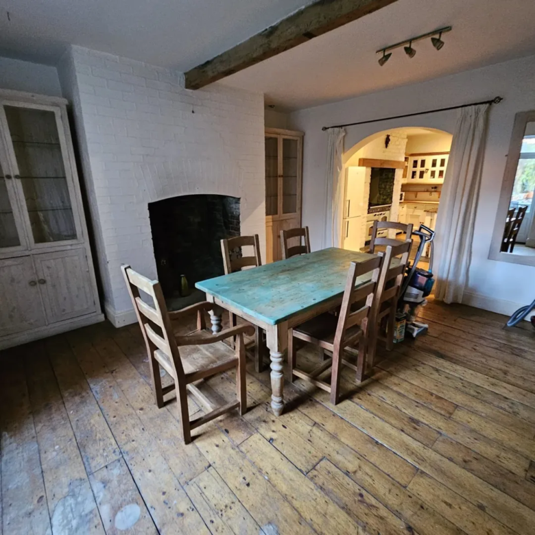 Dining room with rustic table, chairs, fireplace, and wooden floors.