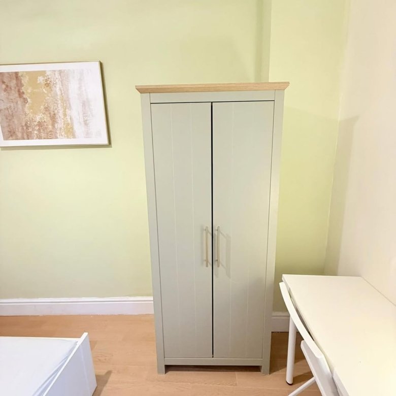 Sage green wardrobe with wooden top next to white desk, bedroom interior.