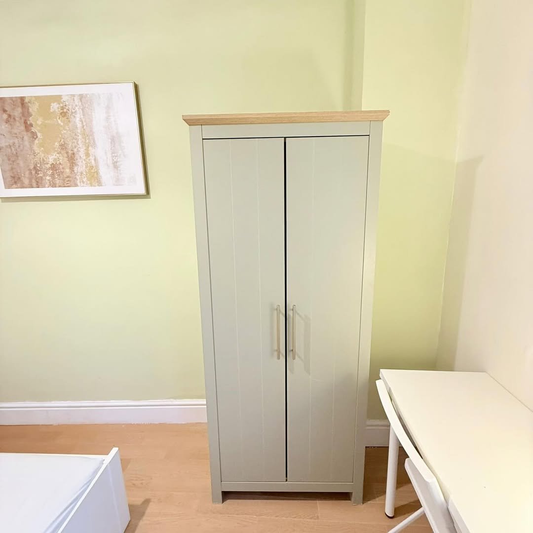 Sage green wardrobe with wooden top next to white desk, bedroom interior.