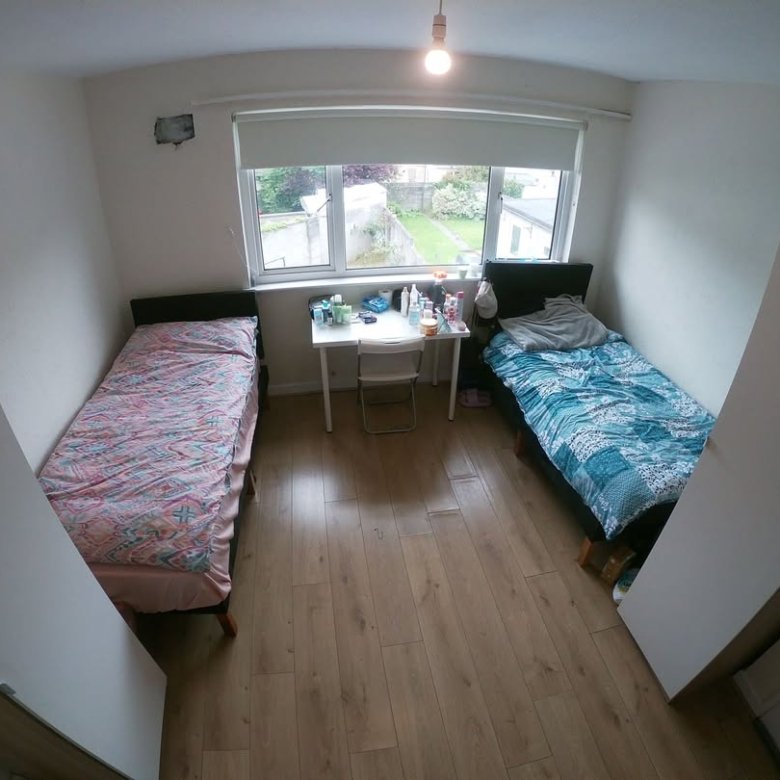 Shared bedroom with two beds, desk, and window overlooking a garden.