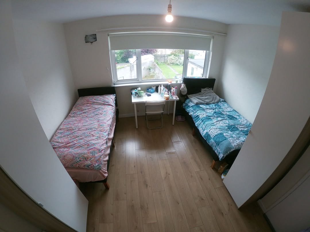 Shared bedroom with two beds, desk, and window overlooking a garden.