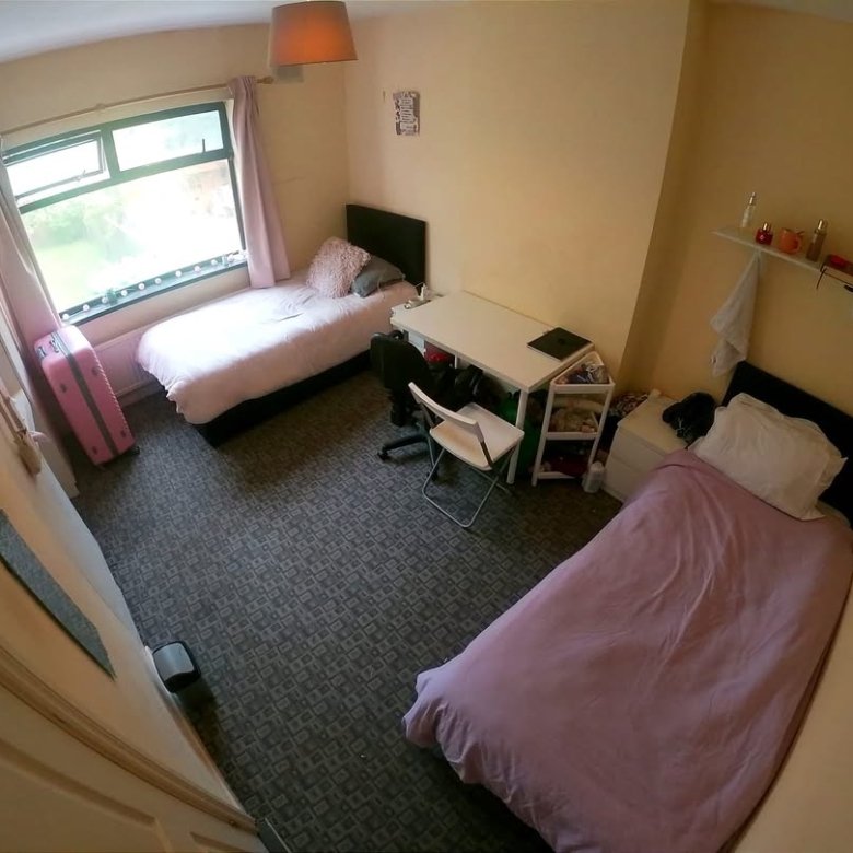 Cozy shared bedroom with two beds, desk, and wardrobe. Natural light from window.