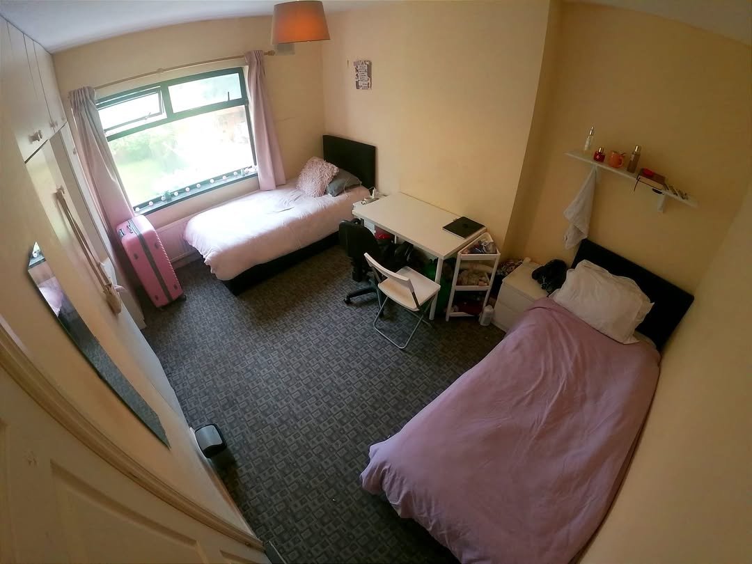 Cozy shared bedroom with two beds, desk, and wardrobe. Natural light from window.