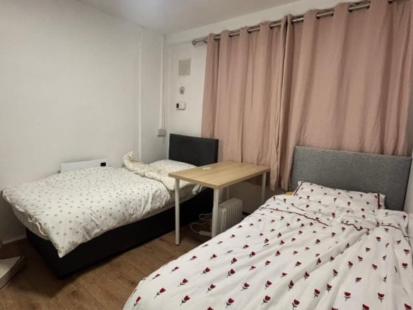 Cozy shared bedroom with two beds, small table, and pink curtains.