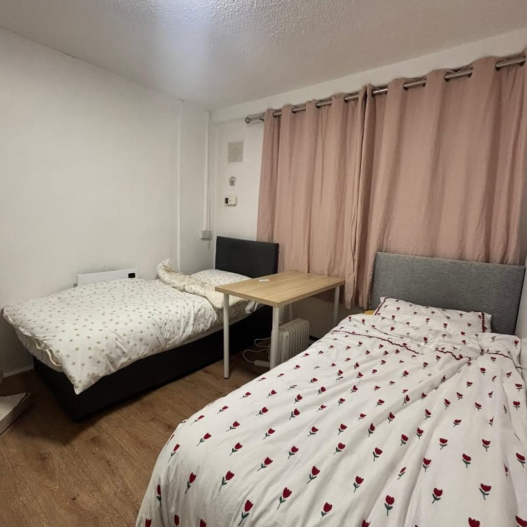 Cozy shared bedroom with two beds, small table, and pink curtains.