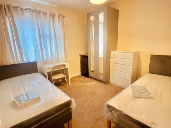 Shared bedroom with two beds, desk, wardrobe, and dresser. Neutral tones.