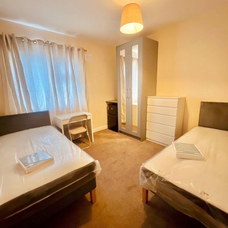 Shared bedroom with two beds, desk, wardrobe, and dresser. Neutral tones.