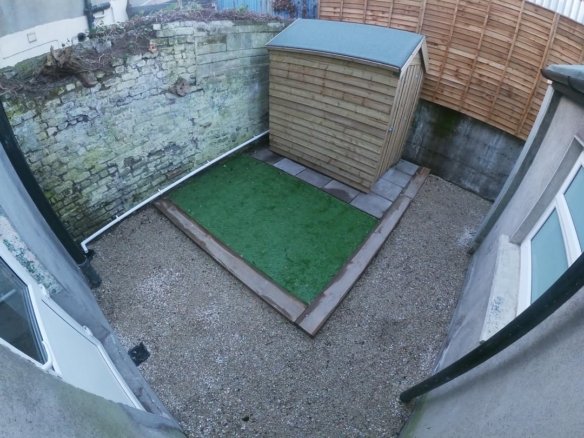 Small backyard with artificial grass, shed, and gravel. Compact outdoor space.