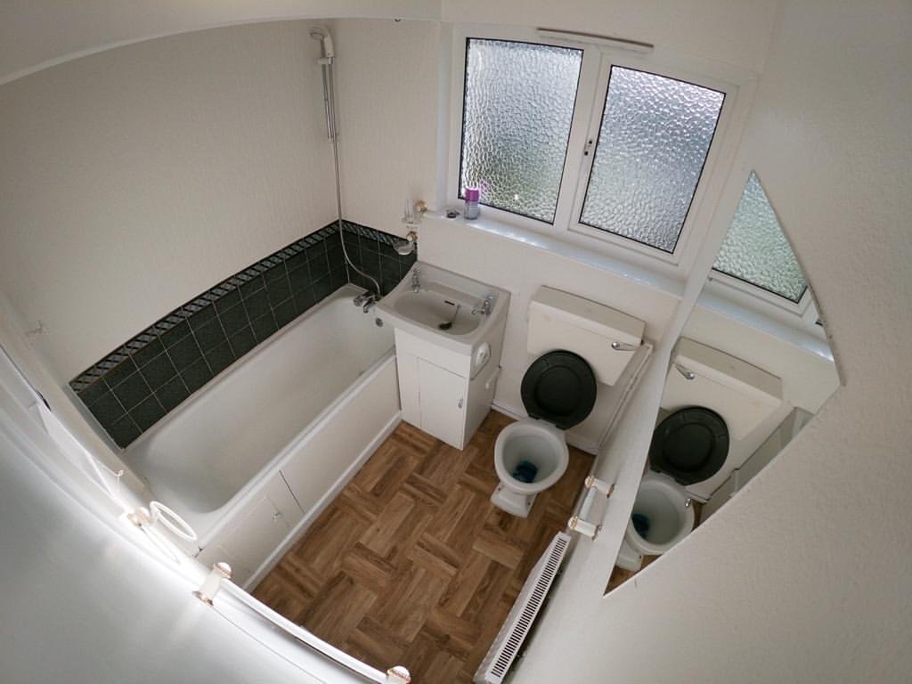 Small bathroom with bathtub, toilet, sink, and window. Herringbone floor.