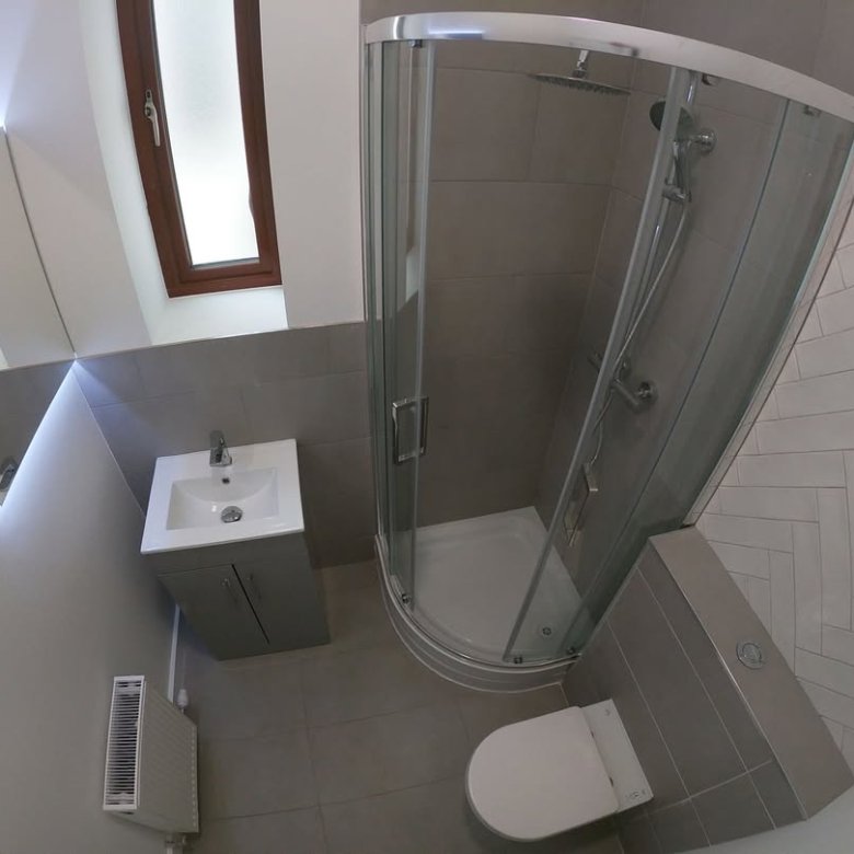 Small bathroom with corner shower, toilet, sink, and window.