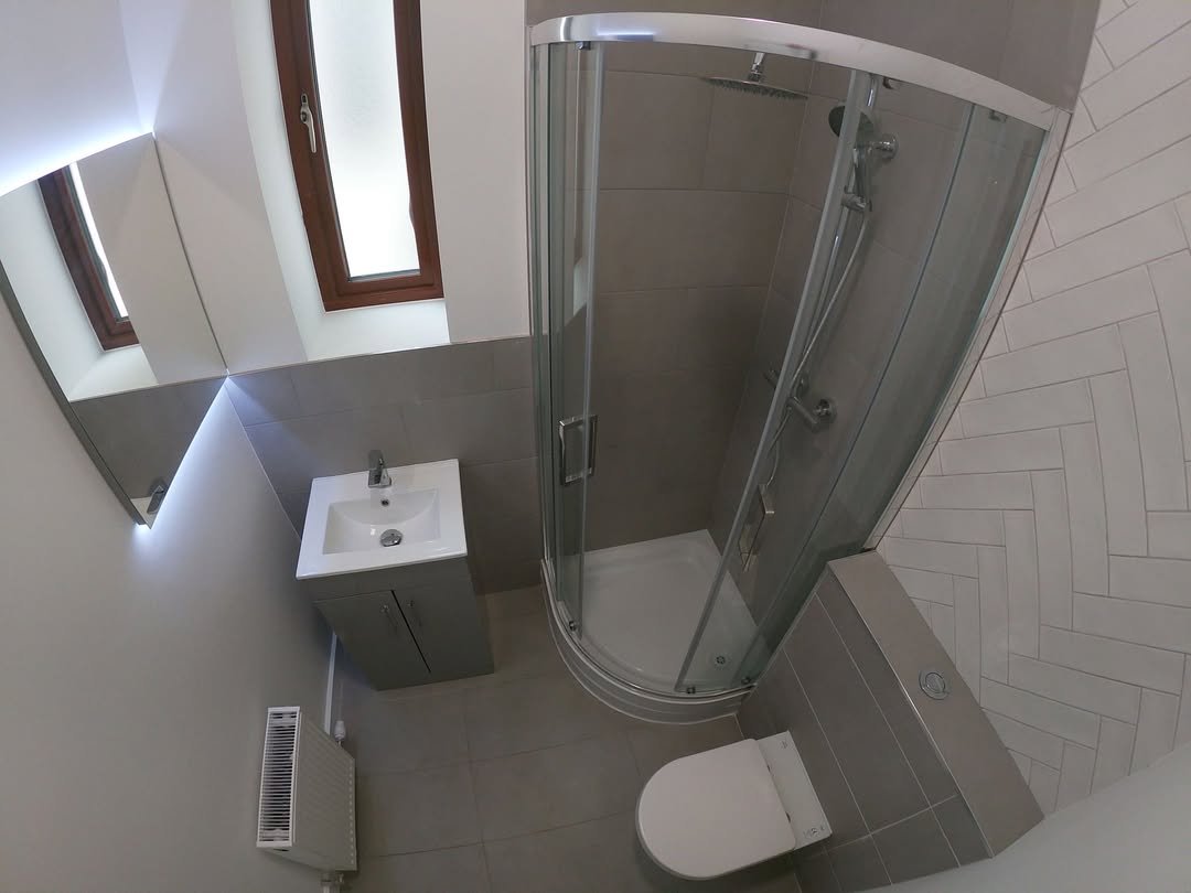 Small bathroom with corner shower, toilet, sink, and window.