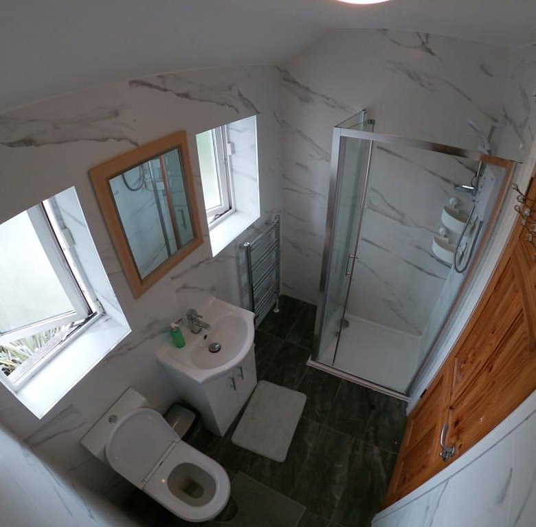 Small bathroom with marble walls, shower, toilet, sink, wood door, and two windows.