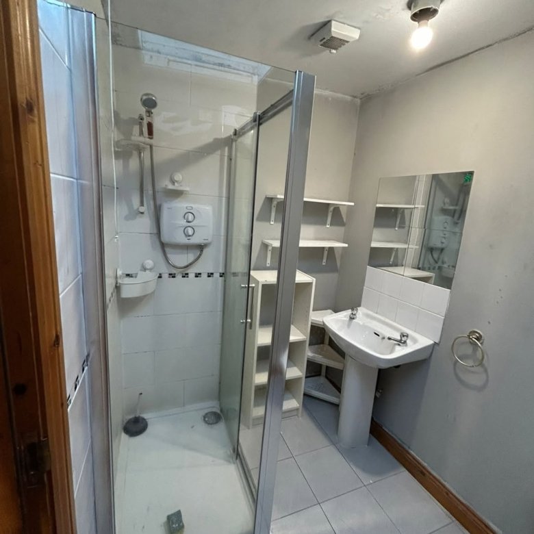 Small bathroom with shower, pedestal sink, shelves, and gray walls.