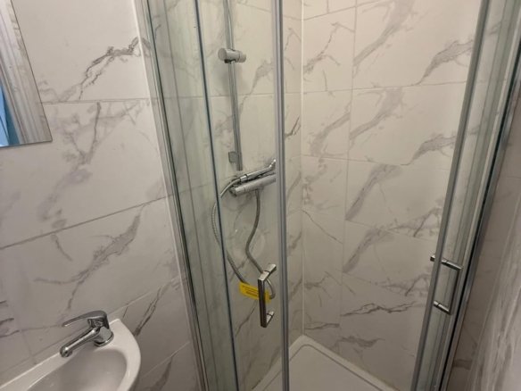 Small bathroom with shower enclosure, sink, and marble-patterned tiles.