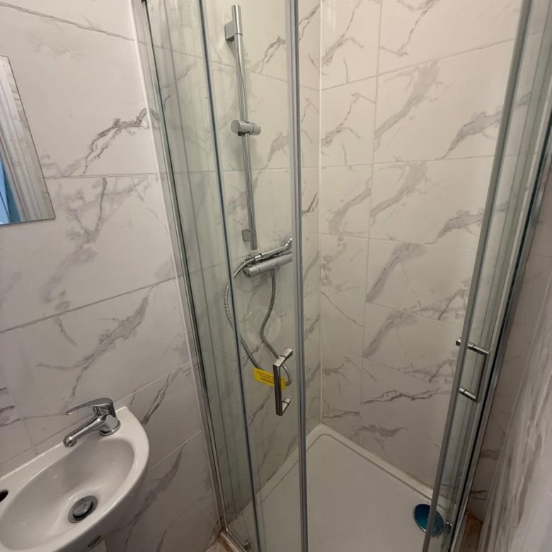 Small bathroom with shower enclosure, sink, and marble-patterned tiles.