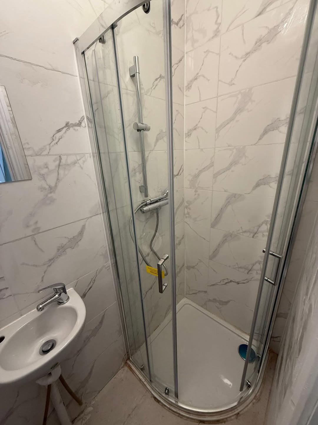 Small bathroom with shower enclosure, sink, and marble-patterned tiles.