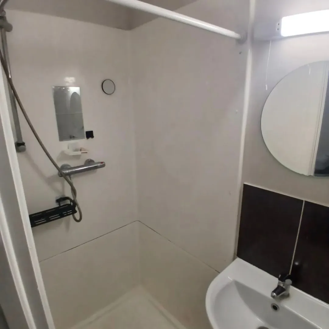 Small bathroom shower with sink, mirror, and white walls.