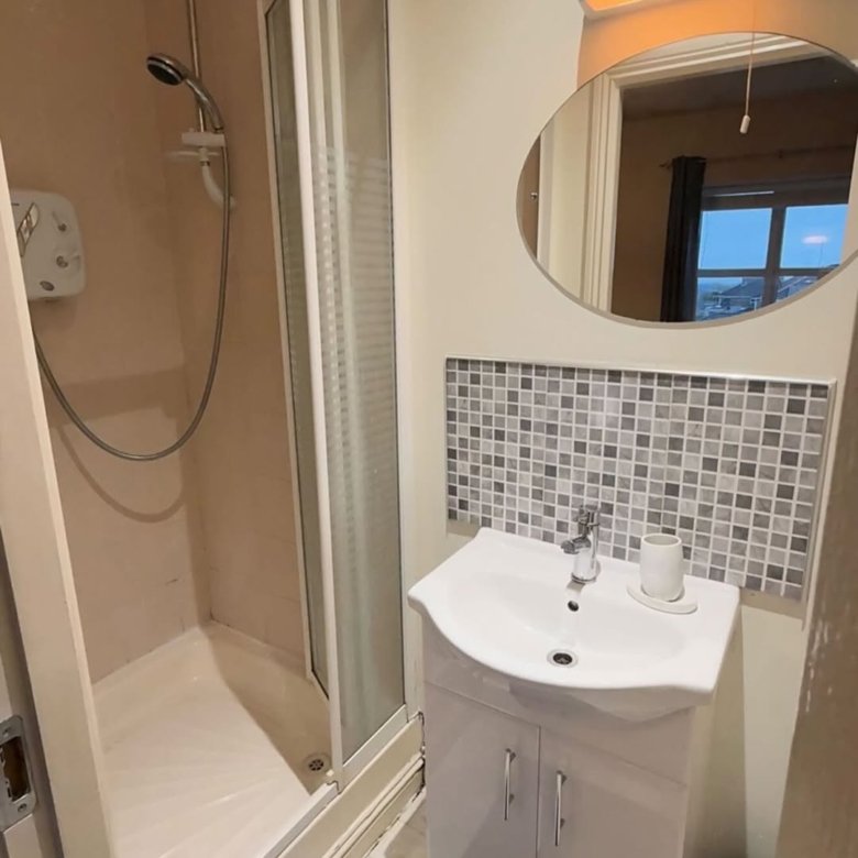 Small bathroom with shower, sink, mosaic tile backsplash, and oval mirror.