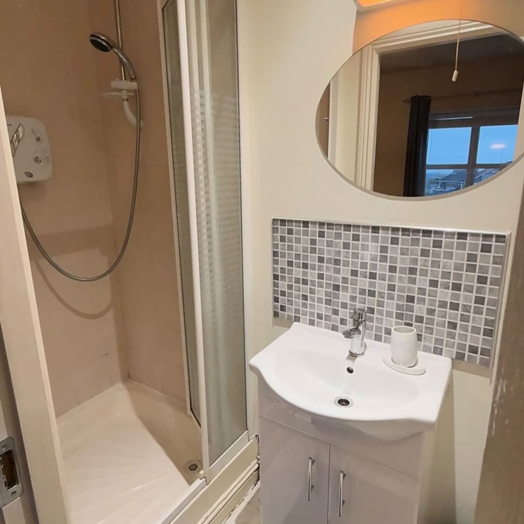 Small bathroom with shower, sink, mosaic tile backsplash, and oval mirror.