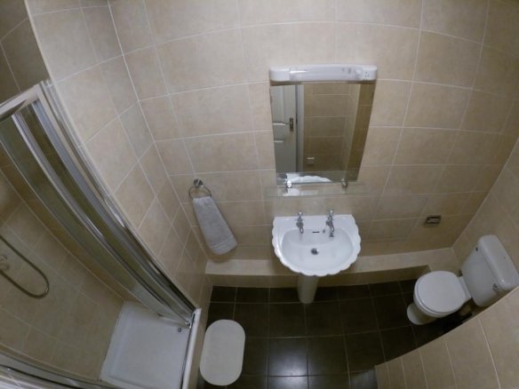 Small bathroom with shower, sink, toilet, and beige tile. Clean, compact design.