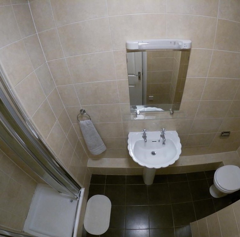 Small bathroom with shower, sink, toilet, and beige tile. Clean, compact design.