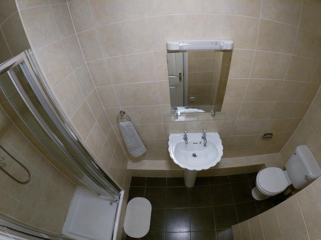 Small bathroom with shower, sink, toilet, and beige tile. Clean, compact design.