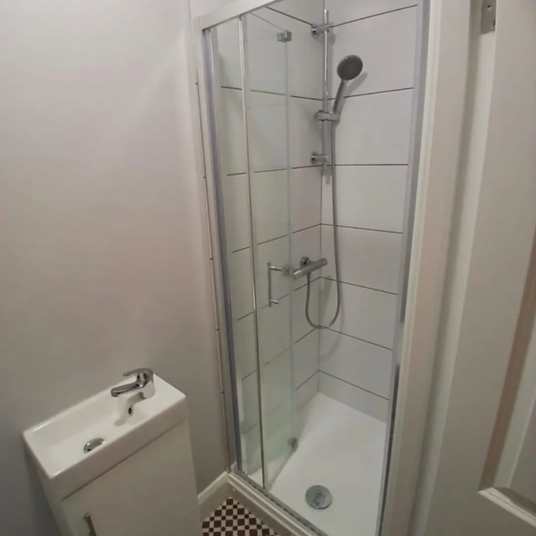 Small bathroom with shower and sink. White tiles and checkered floor.