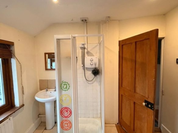 Small bathroom with shower, sink, window and wooden door. Chakra symbols on shower door.
