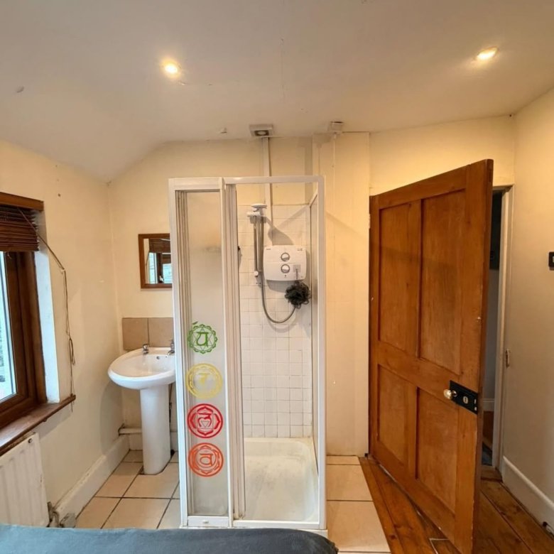 Small bathroom with shower, sink, window and wooden door. Chakra symbols on shower door.