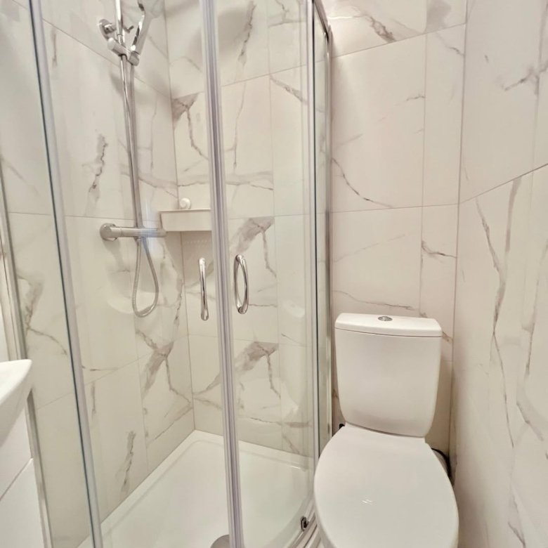 Small bathroom with shower and toilet against marble-patterned tile.