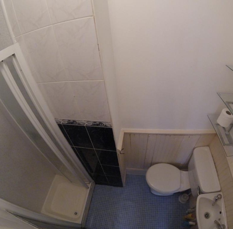 Small bathroom with shower, toilet, sink, and shelves. Blue tile floor, white walls.
