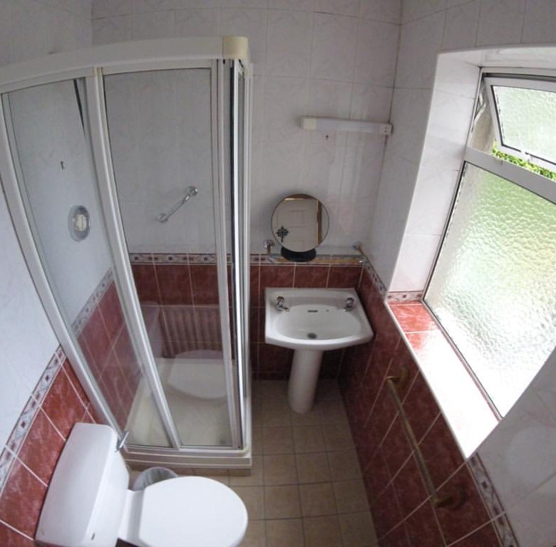 Small bathroom with shower, toilet, sink, and window. Red and white tile.